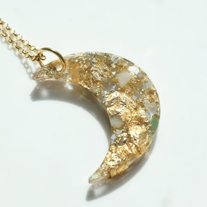 May include: A gold crescent moon necklace with a clear resin pendant filled with gold flakes and white and green stones.