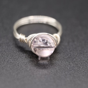 May include: A silver wire wrapped ring with a light pink gemstone.