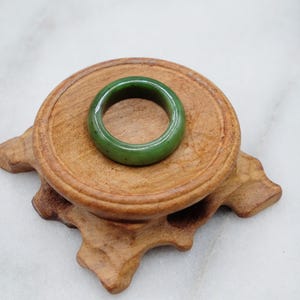 May include: A green jade ring on a wooden stand. The ring is smooth and polished.