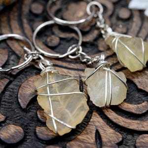 May include: Three silver keychains with clear yellow crystal stones wrapped in silver wire. The stones are different shapes and sizes.