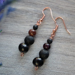 May include: A pair of dangle earrings with black lava rock beads, garnet beads, and copper wire.