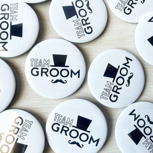 May include: A collection of white round buttons with black text and graphics. The buttons say "Team Groom" with a graphic of a top hat and a moustache.