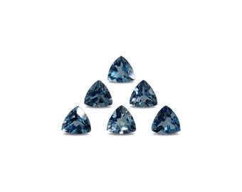 May include: Seven triangular, faceted gemstones in varying shades of blue are arranged in a pyramid shape against a white background. The gems have a polished, reflective surface, showcasing their clarity and color.