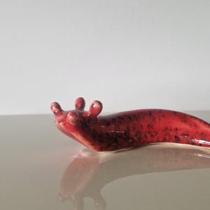 Könnte beinhalten: Keramik-Schneckenfigur in Rot und Dunkelbraun. Die Schnecke hat eine glänzende Oberfläche und ein detailliertes Design mit drei kleinen Antennen. Die Figur ist ein dekoratives Objekt.