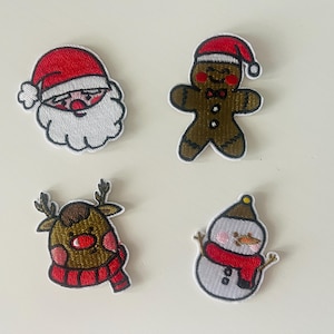 May include: Four embroidered Christmas patches: Santa Claus, a gingerbread man, a reindeer, and a snowman. Each patch has a white border and colourful details. The Santa has a red hat and white beard. The gingerbread man wears a bow tie.