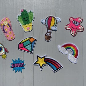 May include: A set of ten colourful iron-on patches featuring a variety of designs, including a cactus, a hot air balloon, a rainbow, a rocket, a star, a diamond, a flip-flop, a starfish, and a speech bubble with the word "OMG!"