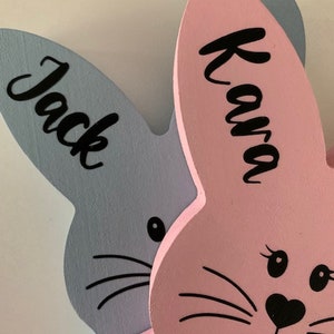 May include: Two wooden bunny rabbit shapes, one light blue with the name "Jack" and one pink with the name "Kava".