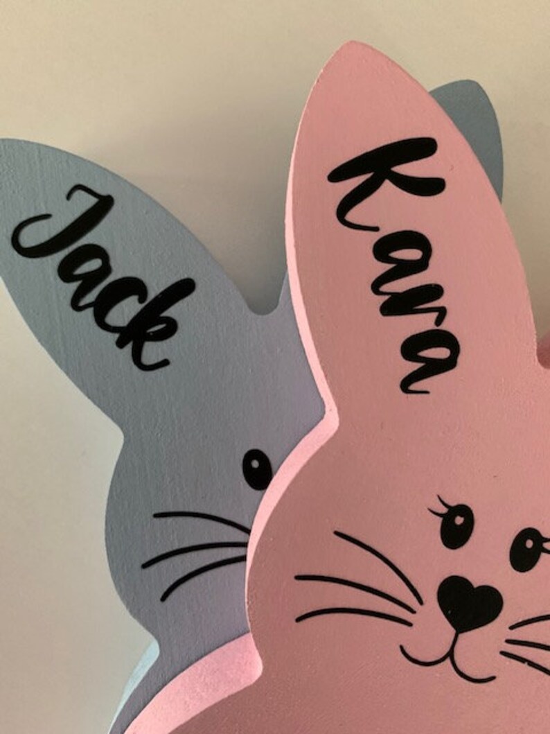 May include: Two wooden bunny rabbit shapes, one light blue with the name "Jack" and one pink with the name "Kava".