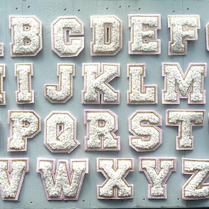 May include: White felt alphabet letters with pink and gold trim. Each letter is individually cut out and has a fluffy texture.