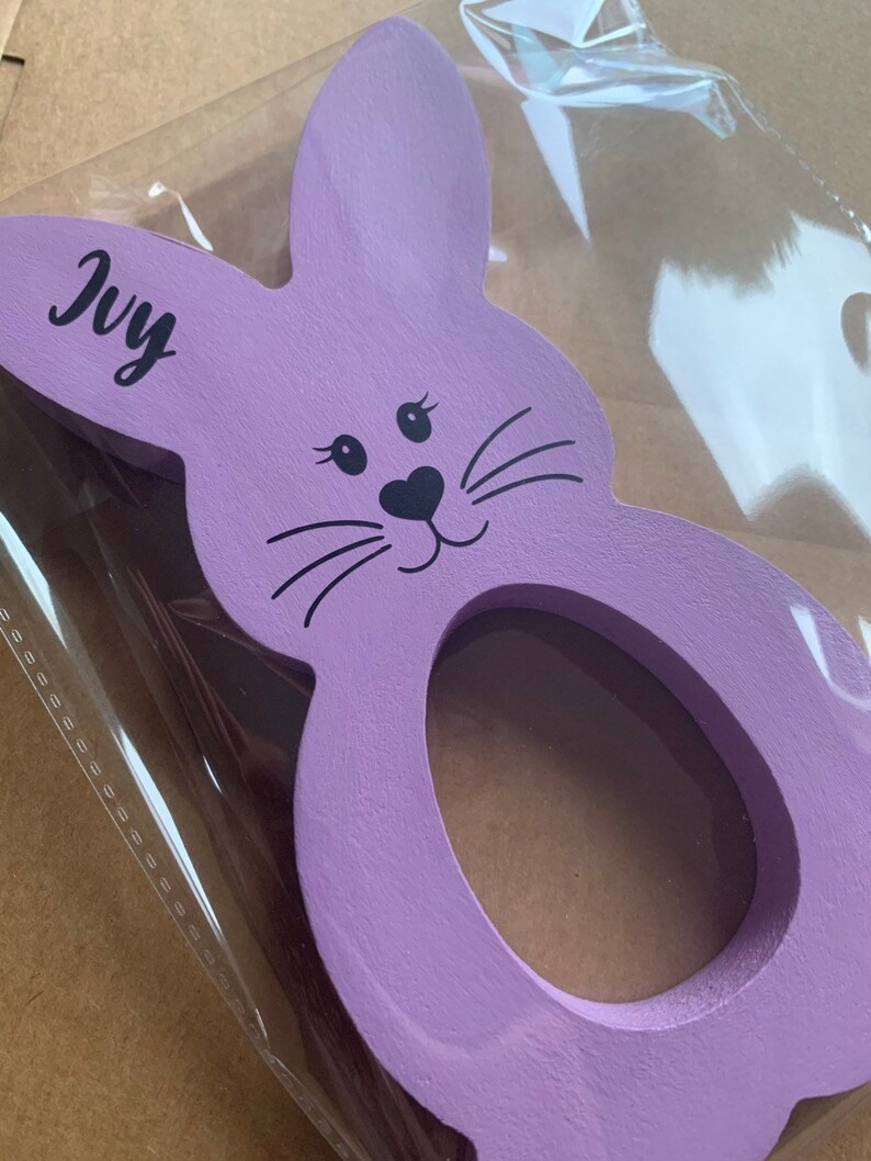 May include: Purple wooden bunny rabbit egg holder with a black face and whiskers. The bunny has a hole in the middle for an egg. The bunny has the name "Ivy" written on it.