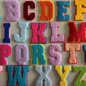 May include: A set of 26 colourful felt letters, each letter is a different colour and has a fuzzy texture. The letters are arranged in alphabetical order.