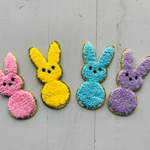 May include: Four felt bunny shaped Easter decorations. One is yellow, one is blue, one is pink, and one is purple.