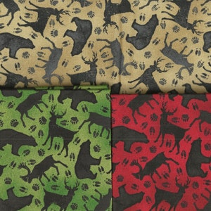 May include: Fabric squares with a repeating pattern of black bears, deer, and paw prints. The fabric is available in tan, green, and red. The fabric is suitable for quilting, sewing, and crafting projects.