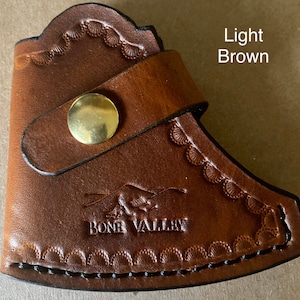 May include: Light brown leather axe sheath with a decorative stitch pattern and a brass button. The sheath has the words "Bone Valley" embossed on the front.