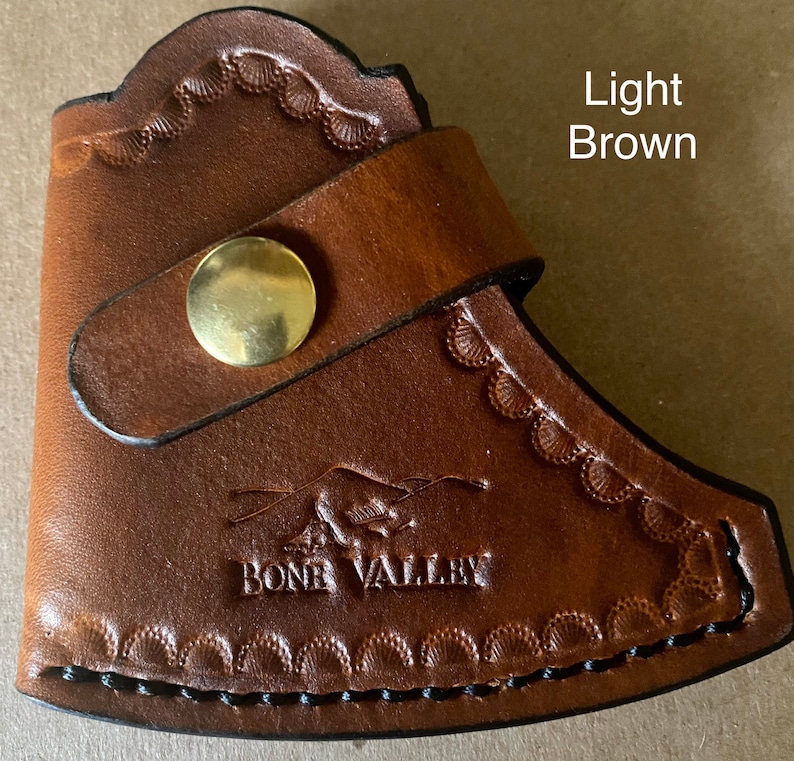 May include: Light brown leather axe sheath with a decorative stitch pattern and a brass button. The sheath has the words "Bone Valley" embossed on the front.