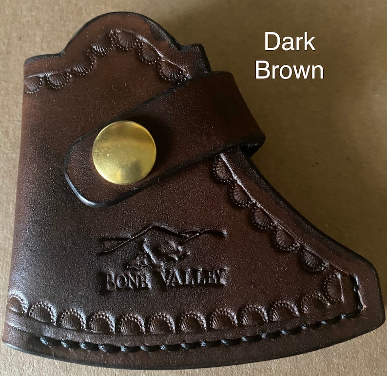May include: Dark brown leather axe sheath with a snap closure and a decorative embossed design. The sheath has the text "Bone Valley" embossed on the front.