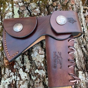 May include: A brown leather axe sheath with a decorative coin and the text "Pike Trail" embossed on the side. The sheath has a lace-up design on the back.