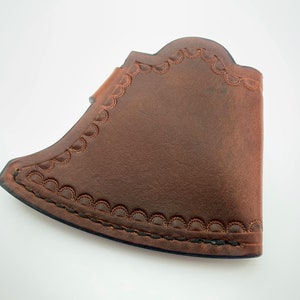 May include: A brown leather axe sheath with a decorative stitched edge.