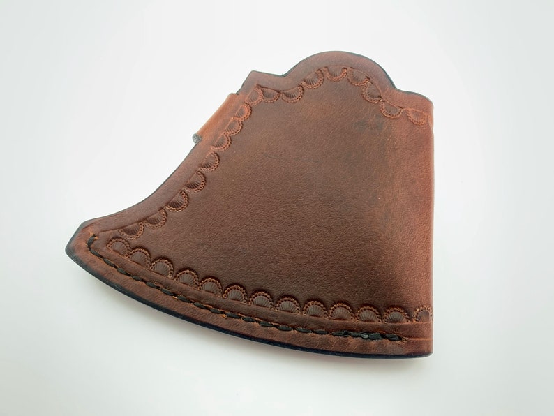 May include: A brown leather axe sheath with a decorative stitched edge.