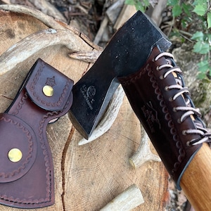 May include: A brown leather sheath with a brass button and a black axe head with a brown leather handle and a white lace detail. The axe head has the text "Made in Switzerland" on it.
