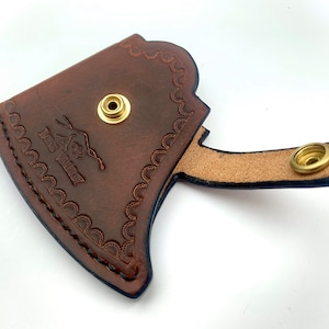 May include: Brown leather axe sheath with a decorative stitched border and a brass snap closure. The sheath has the text "Fox Valley" embossed on the front.