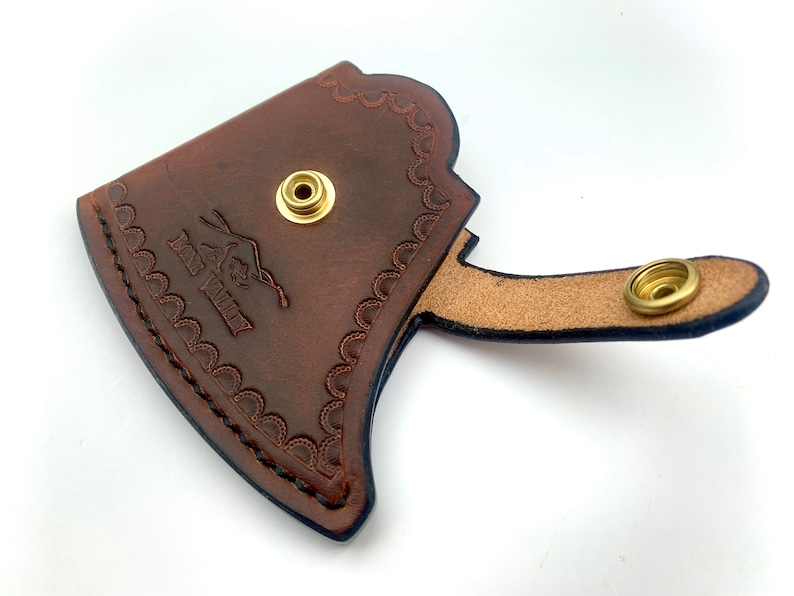 May include: Brown leather axe sheath with a decorative stitched border and a brass snap closure. The sheath has the text "Fox Valley" embossed on the front.