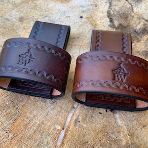 May include: Two brown leather belt loops with a decorative embossed design and the initials "BV" in the center.