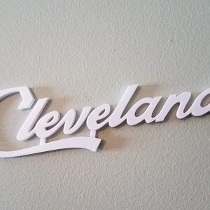 Puede incluir: Un letrero blanco en tres dimensiones en escritura cursiva que dice "Cleveland".