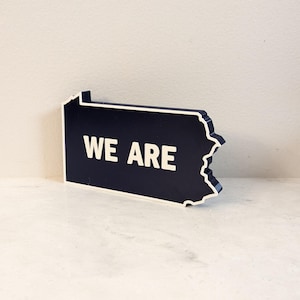 Letrero de escritorio con la palabra WE ARE de Penn State