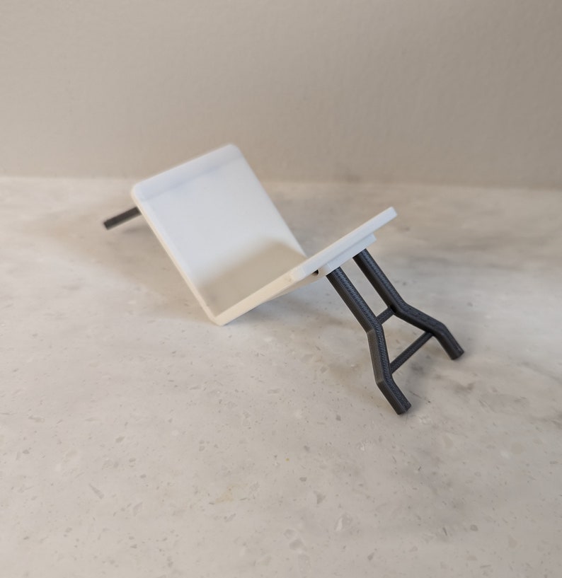 K&ouml;nnte beinhalten: Ein wei&szlig;er, kleiner Klapptisch mit schwarzen Metallbeinen. Der Tisch ist zusammengeklappt und liegt auf der Seite.