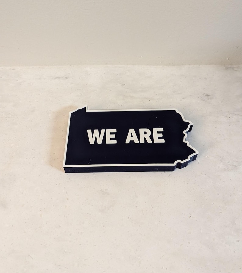 May include: A black outline of the state of Pennsylvania with the words "WE ARE" in white lettering.