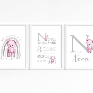 May include: Three white framed prints with a gray and pink color scheme. The first print features a rainbow with a pink teddy bear and the text "Welcome to the world Nova Smith". The second print features a large letter N with a pink teddy bear and the text "Nova Louise Smith 8lb 2oz Tuesday 8th January 2021 49.9 cm 6:21 AM". The third print features a large letter N with a pink teddy bear and the text "N is for Nova".