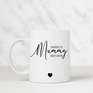 May include: White ceramic mug with a black inscription that reads "Daniel's Mummy Est 2018" and a small black heart.
