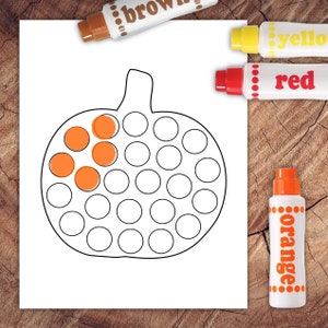May include: A white paper with a black outline of a pumpkin, partially filled with orange circles. Markers labeled "brown", "yellow", "red", and "orange" are arranged around the paper on a wooden surface. The orange marker is visible.