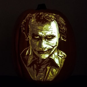 May include: A carved pumpkin with a portrait of the Joker from the movie "The Dark Knight". The face is illuminated with a warm, yellow light, creating a spooky Halloween decoration. The pumpkin is orange.