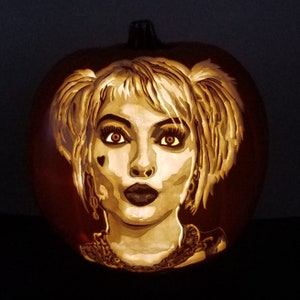May include: A carved pumpkin with a detailed depiction of Harley Quinn, a popular comic book character. The pumpkin is lit from within, illuminating the intricate details of the carving.