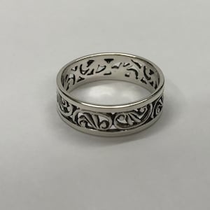 Op de afbeelding: Een zilveren bandring met een decoratief, ingewikkeld, uitgesneden ontwerp.