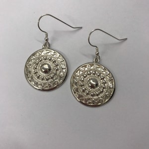 May include: A pair of silver earrings with a circular design. The earrings have a hook fastening and a detailed pattern of circles and swirls.