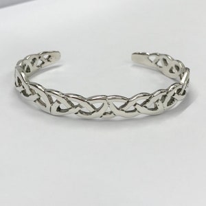 May include: A silver Celtic knot bangle bracelet. The bracelet is made from a single piece of metal that is woven into a complex pattern.