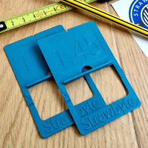 Puede incluir: Dos soportes de números de plástico azul turquesa con el número 1,45 impreso en ellos. Los soportes están etiquetados como "Strawbyte".
