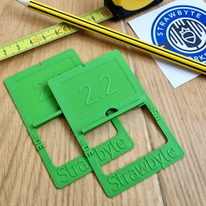 May include: Two green plastic phone stands with the text "Strawbyte" and the number "2.2" printed on them.