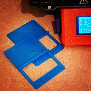 Puede incluir: Dos soportes de plástico azul impresos en 3D con la palabra "Stand Up" impresa en ellos. Los soportes están diseñados para sostener objetos pequeños.