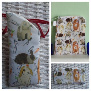 May include: A white glasses case featuring a bunny and carrot pattern, holding red glasses. A matching zippered pouch and a smaller pouch, both with the same bunny design, are also visible in the image.