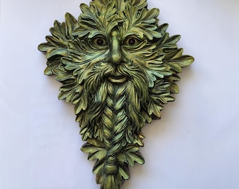 Könnte beinhalten: Eine Wandplakette mit einem Green-Man-Motiv, gestaltet mit komplexen Schichten aus überlappenden Eichenblättern in Waldgrün- und Goldtönen. Das Gesicht ist in das Laub integriert und weist einen geflochtenen Bart sowie dunkle Augen auf.