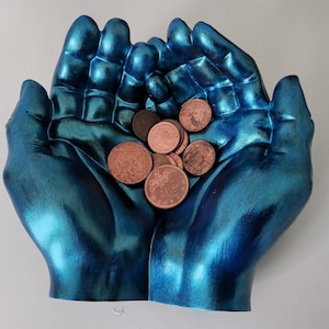 May include: A pair of blue hands holding a pile of copper-colored coins. The hands are made of a smooth, metallic material.