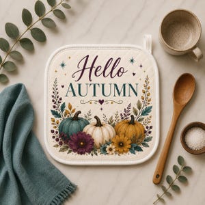 May include: A square quilted pot holder in cream fabric featuring the text Hello AUTUMN in dark purple and green. The design includes illustrations of three pumpkins in teal, white, and orange, surrounded by colorful autumn flowers and foliage.