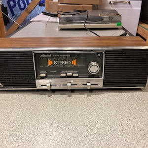 May include: A vintage Masterwork AM/FM stereo receiver featuring a rectangular wood grain cabinet, black speaker grilles, and a central control panel with silver knobs, push buttons, and sliding switches. The display shows the text STEREO.