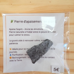 Könnte beinhalten: Ein grauer Granitstein mit der Aufschrift "Pierre d'apaisement en granit" und einem Text, der seine Eigenschaften und Verwendungen beschreibt. Der Text enthält "Apaise l'esprit - Ancre les émotions", "Pierre naturelle à frotter entre le pouce et l'index pour calmer le stress", "Le granit aide à retrouver calme, stabilité et patience", "Idéale pour se reconnecter à la nature", "Purification: eau", "Rechargement: lumière du soleil ou contact avec la Terre", und "5€".