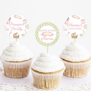May include: Three cupcakes with white frosting topped with round paper cupcake toppers. The toppers feature a spa theme with illustrations of cucumbers, bath bombs, and a pink eye mask. The text on the toppers reads "Pamper Party", "Happy B-Day Olivia", and "Olivia's 8th B-Day".