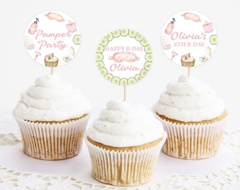 May include: Three cupcakes with white frosting topped with round paper cupcake toppers. The toppers feature a spa theme with illustrations of cucumbers, bath bombs, and a pink eye mask. The text on the toppers reads "Pamper Party", "Happy B-Day Olivia", and "Olivia's 8th B-Day".